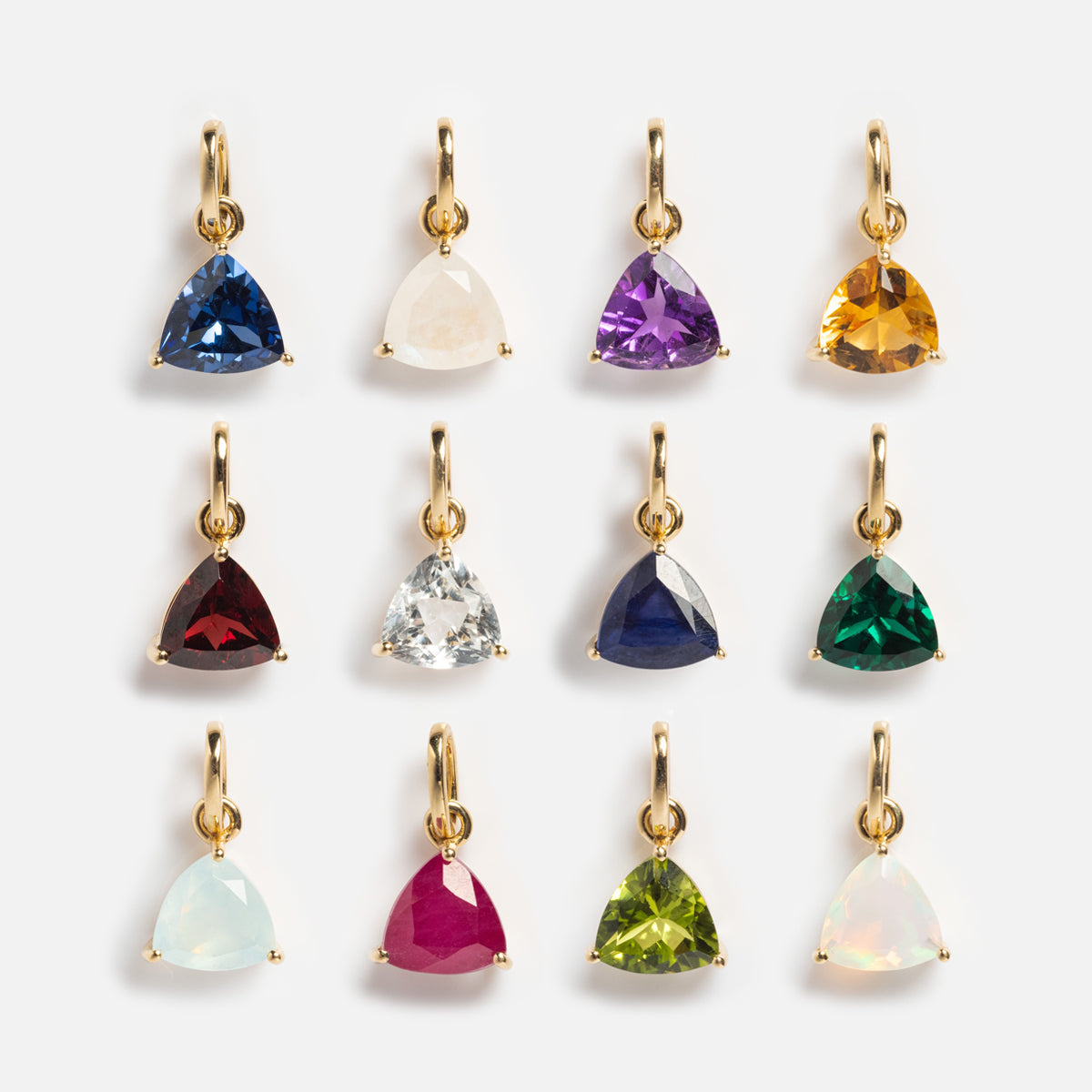 Twelve Family Gold Solid Gold Trillion Birthstone Charms with vibrant trillion-cut gemstones—blue, purple, yellow, pink, light green, and an iridescent personalized charm—are arranged in three rows on a white background.