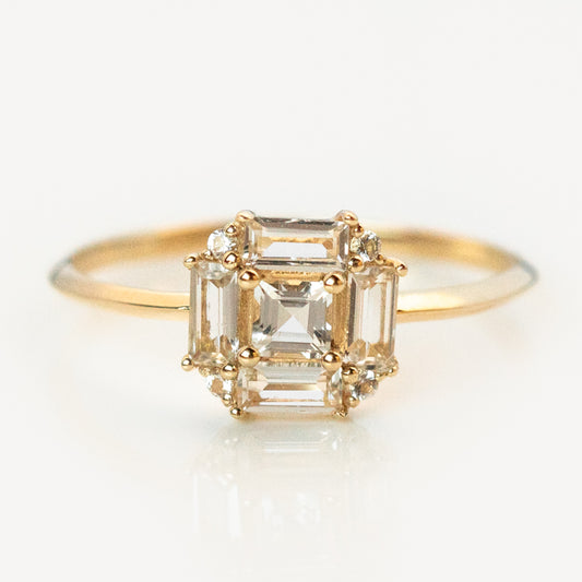 The 14k Vintage Inspired Art Deco Engagement Ring features a central emerald-cut diamond, smaller rectangular diamonds in prong settings, and a thin band—all crafted from recycled gold.