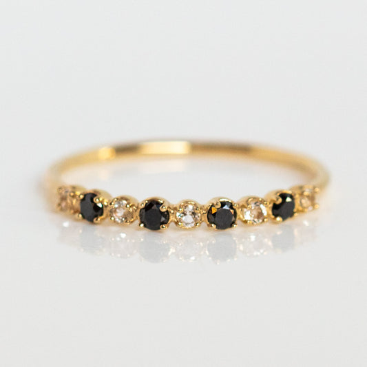 The 14k Classic White Sapphire and Black Diamond Band features alternating black diamonds and white sapphires in yellow gold, displayed on a white surface.