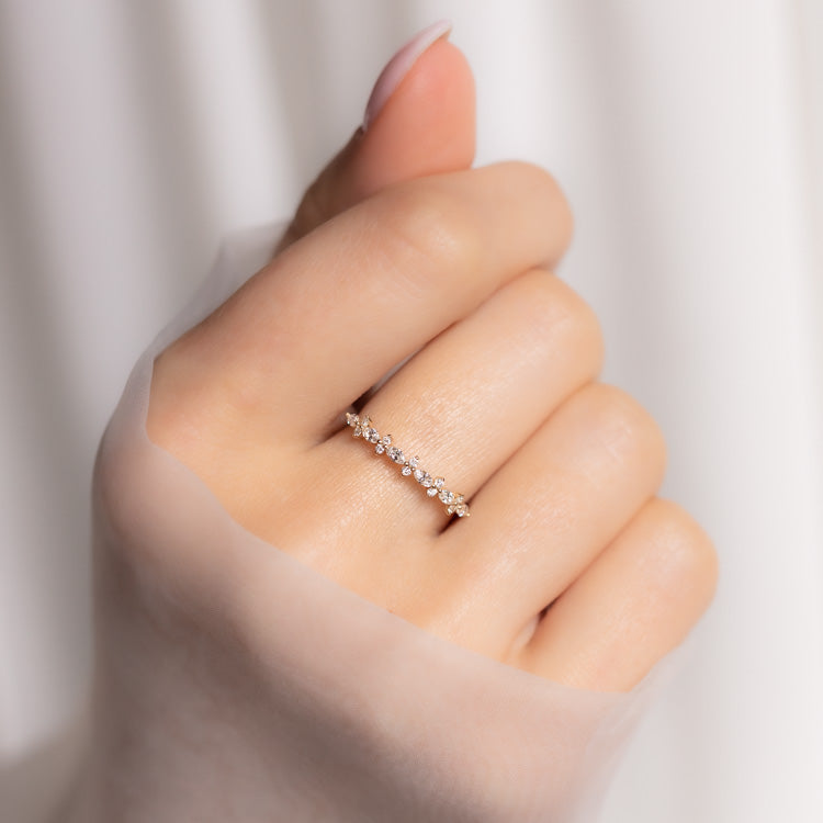 A hand with manicured nails wears the 14k Luxe Diamond Celebration Band (Sample Size 7), a delicate gold ring adorned with small diamonds, softly draped in sheer white fabric against a blurred white background.