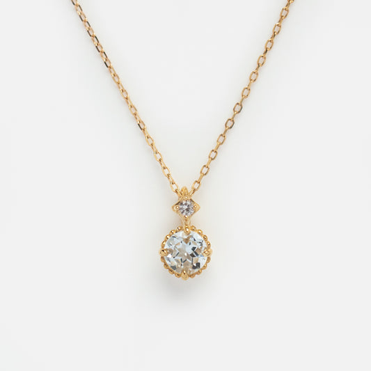 The Solid Gold Something Blue Aquamarine Necklace features a round, faceted aquamarine pendant with a smaller gemstone above it—an elegant choice for wedding jewelry, shown against a white background.