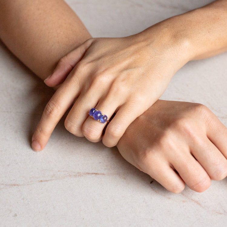 A close-up of two hands on a light surface, with one hand wearing the Sweetest Gumdrop Ring—a chunky, purple beaded ring crafted from natural gemstones—on the middle finger.