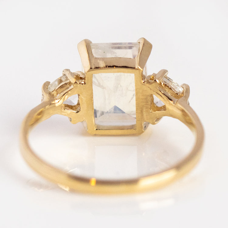The Empress Moonstone Ring is crafted in 14k yellow gold, featuring a large rectangular moonstone centerpiece flanked by two smaller stones on each side, all set within an ornate band and displayed against a white background.