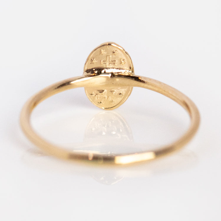 The Tiny Miraculous Medal Ring is a delicate 14k gold piece with an oval flat top engraved with a small cross and multiple stars, symbolizing religious protection, shown against a plain white background.