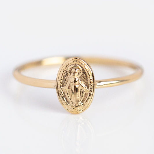 The Tiny Miraculous Medal Ring is a delicate 14k gold piece featuring an oval Virgin Mary medal engraved on a thin band, symbolizing religious protection. Shown against a white background.