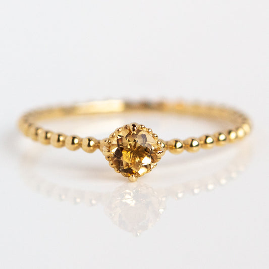 The Solid Gold Sunny Citrine Ring features a delicate beaded solid gold band with a small, round citrine gemstone set at the center, displayed on a white background.