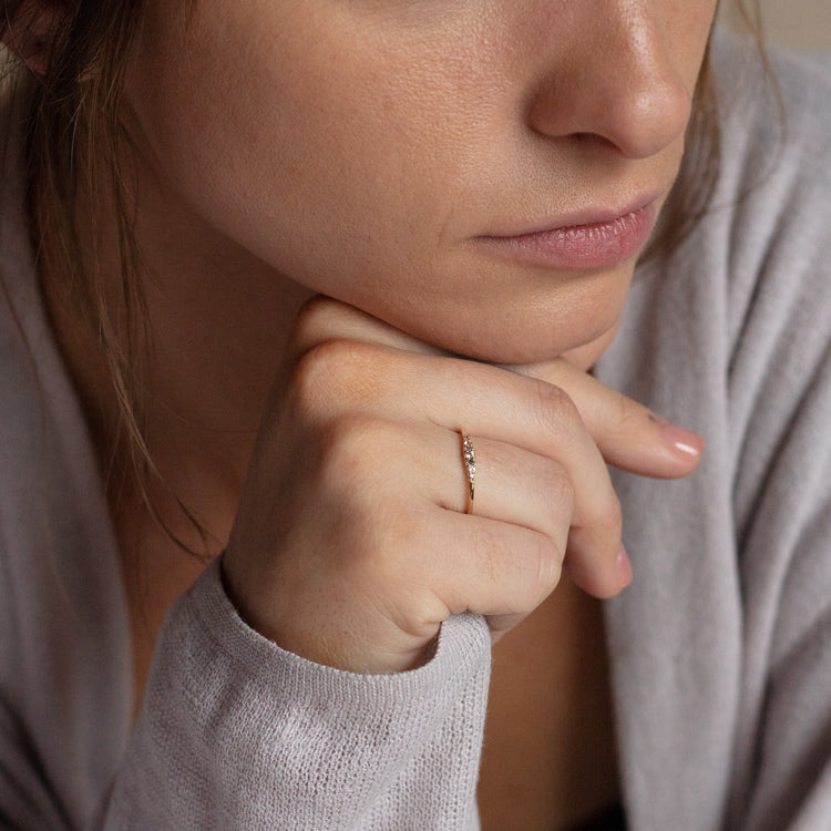 A woman in a light gray sweater, with a contemplative look, rests her chin on her hand and displays the Solid Gold Classic Salt and Pepper Diamond Ring featuring white sapphires on her finger.