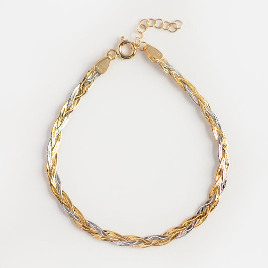 The Solid Gold Mixed Metal Braided Bracelet features intertwined white and yellow gold strands in a herringbone pattern, with a lobster clasp and adjustable extension chain, shown on a white background.