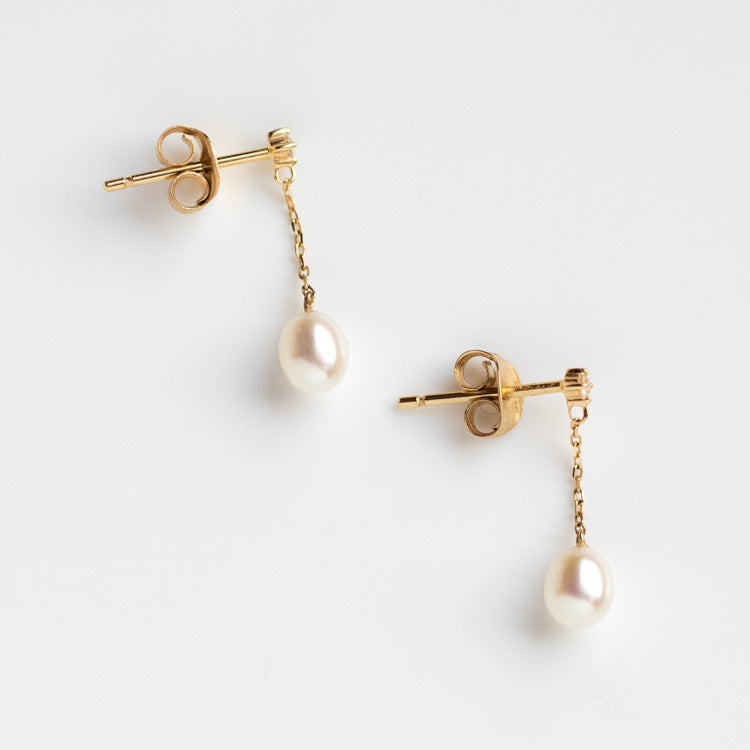 Solid Gold Pearl and White Sapphire Drop Earrings featuring gold studs, delicate chains, a single freshwater pearl drop on each, displayed on a white background.
