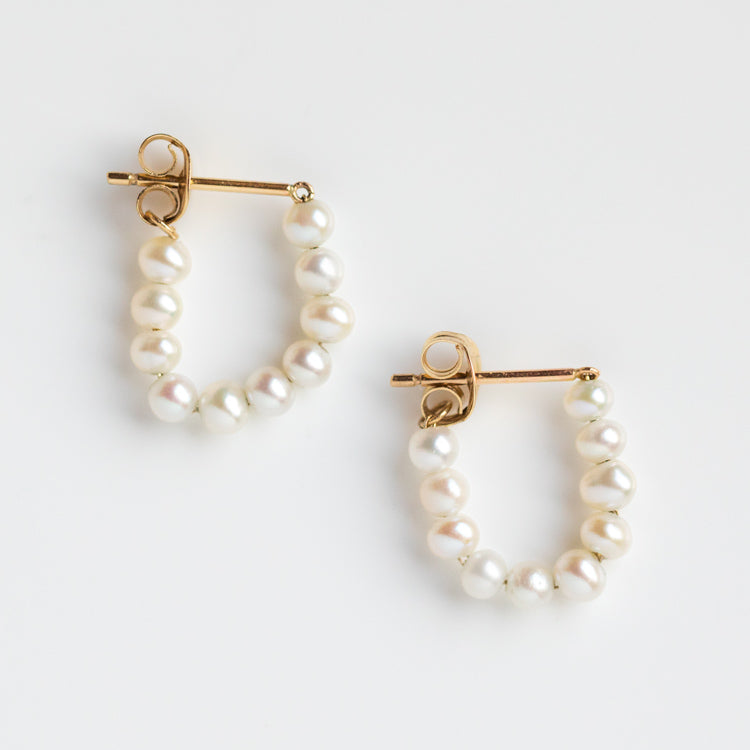 The Solid Gold Pearl Strand Hoops feature small freshwater pearls along the lower half of each gold hoop, showcased on a white background—an elegant update on classic pearl earrings.
