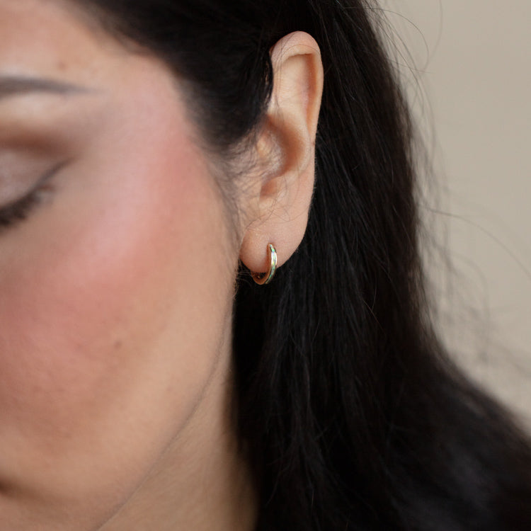 A close-up of a woman's ear adorned with Solid Gold Opal Inlay Huggie Hoops Sample earrings.