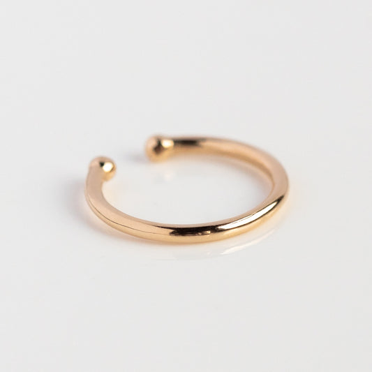 The Solid Gold Essential Ear Cuff features a simple design with rounded ends and rests on a white surface, making it perfect for adding to your ear stack.