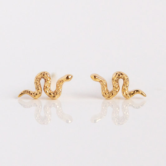 Solid Gold Slither Snake Studs—small, textured snake earrings in solid gold, shown on a reflective white background—perfect for adding a unique twist to your ear stack.