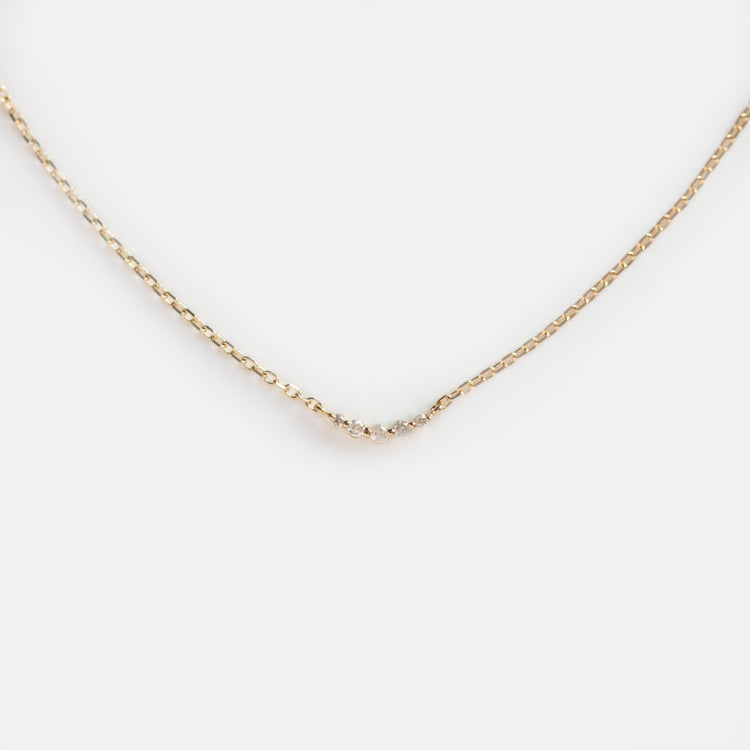 The Solid Gold Diamond Arc Necklace features a delicate gold chain with a small curved row of diamonds at the center, evoking a constellation-like look and displayed on a white background.