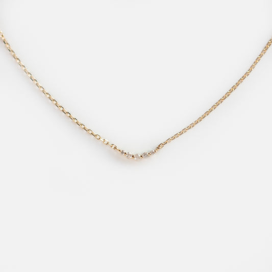 The Solid Gold Diamond Arc Necklace features a delicate gold chain with a small curved row of diamonds at the center, evoking a constellation-like look and displayed on a white background.
