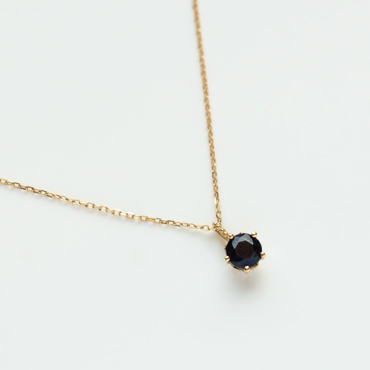 The Solid Gold Blue Sapphire New Moon Necklace for Intuition features a delicate gold chain with a small, round blue sapphire pendant in a simple prong setting, shown against a plain white background.