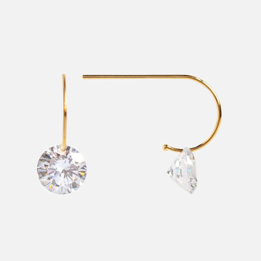 The Floating Solitaire CZ Huggie Earrings are minimalist yellow gold vermeil earrings, each with a single round clear CZ drop hanging below the hook, shown against a plain, light background.