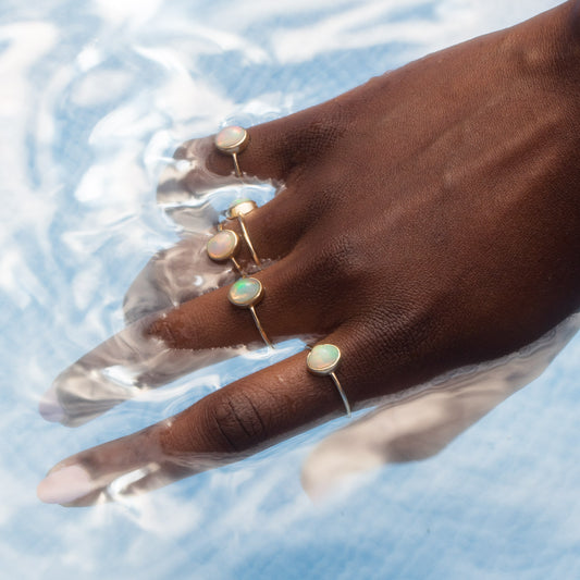 hand in water wearing opal solid gold rings