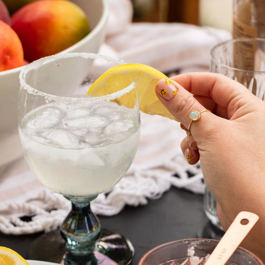 hand with solid gold opal ring placing a lemon wedge on a cocktail