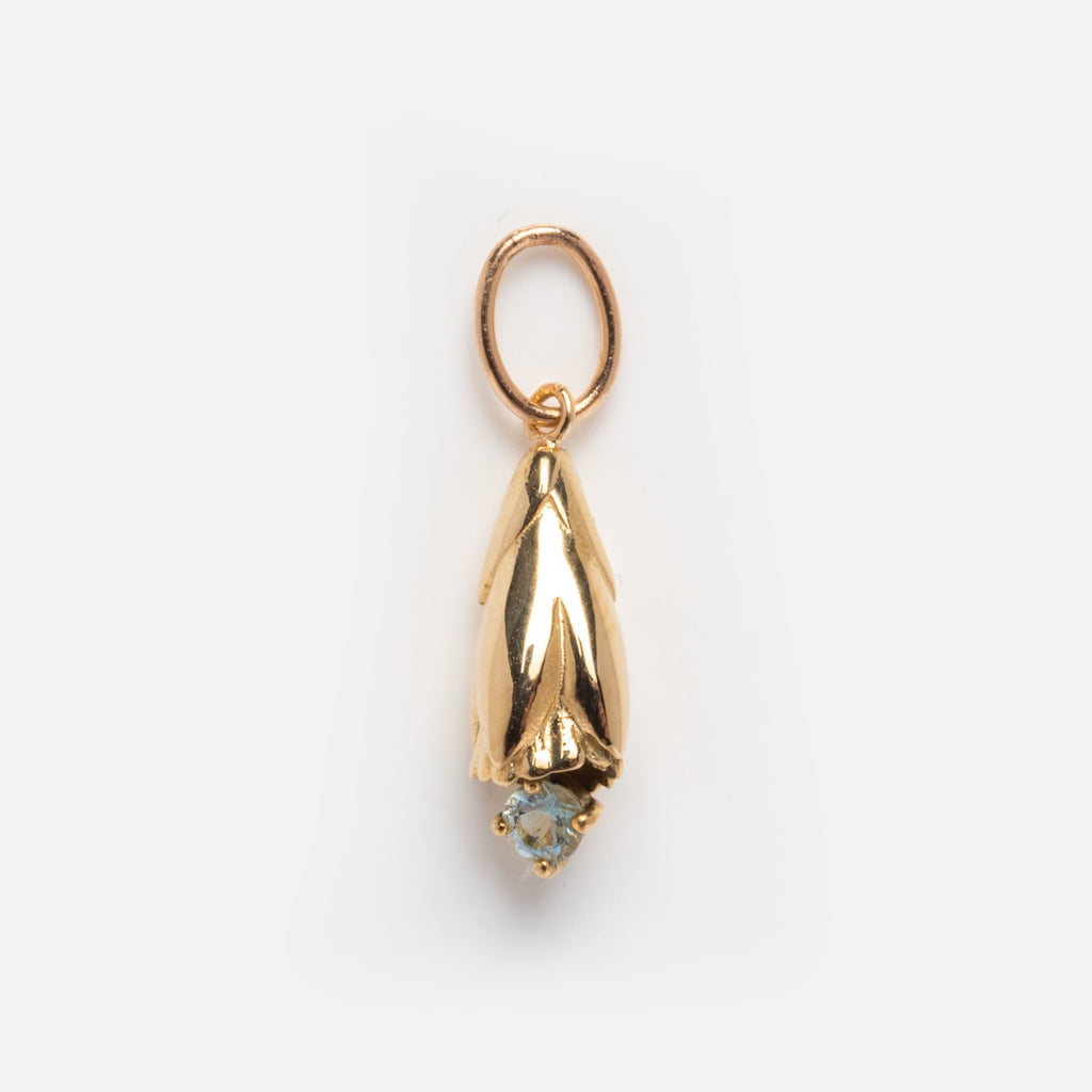 The Solid Gold Birth Flower Bud Charm features a small, gold pendant shaped like a downward-facing flower bud with a round light blue gemstone tip, shown against a white background.