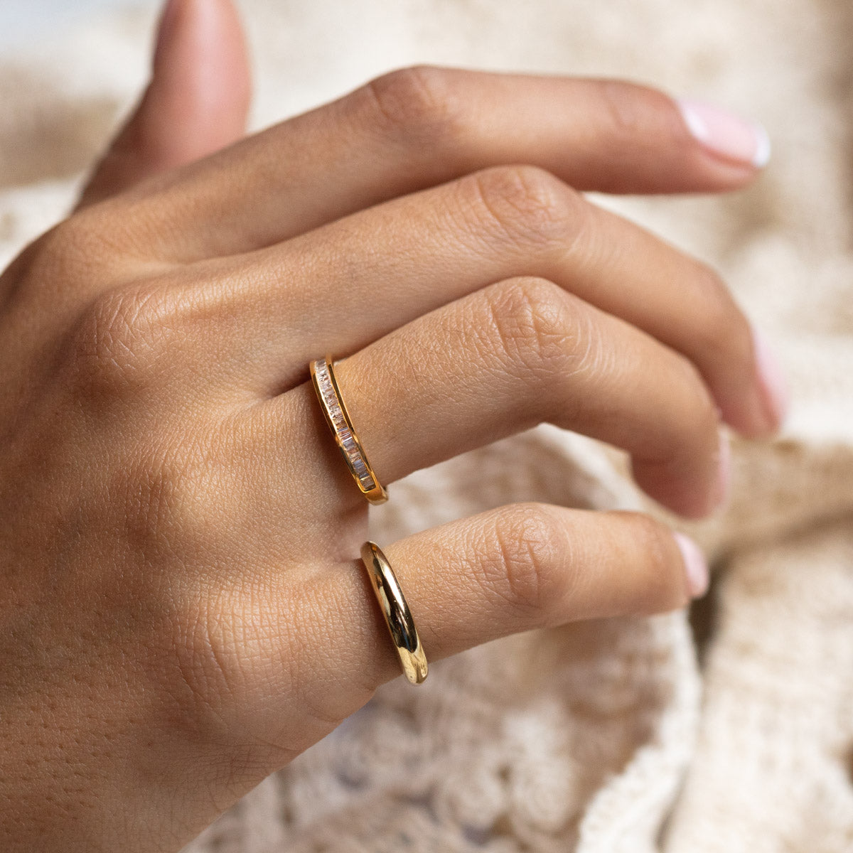 A close-up of a hand with manicured nails, wearing the Pinky Promise Ring in Gold—a sleek, minimal ring—on the pinky finger, set against a textured beige fabric background.