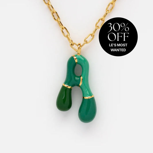 The Bubble Letter Necklace features a gold chain with a glossy green abstract pendant, two teardrop ends, and a central cutout. A black circular label reads "30% OFF LES MOST WANTED," adding playful style to your look.