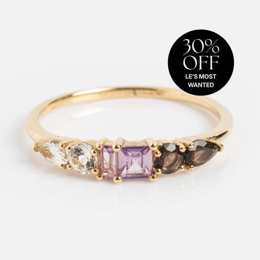 The Solid Gold Modern Ombre Birthstone Ring features five gemstones in different shapes and colors—clear, pink, and smoky. Ideal for stacking or as a unique birthstone ring. A black label reads "30% OFF LES MOST WANTED.