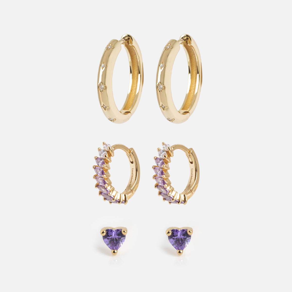 The Bold Birthstone Earring Set features three pairs—gold hoops with small diamonds, gold hoops with purple gemstones and diamonds, and purple heart-shaped studs—arranged vertically on a white background.
