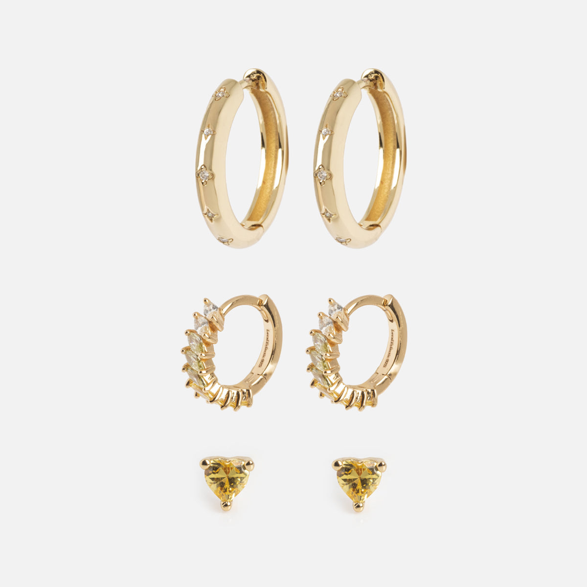 The Bold Birthstone Earring Set features three pairs of gold earrings: simple hoops with small gems, gem-lined hoops, and yellow heart-shaped stud earrings. All are displayed against a white background.