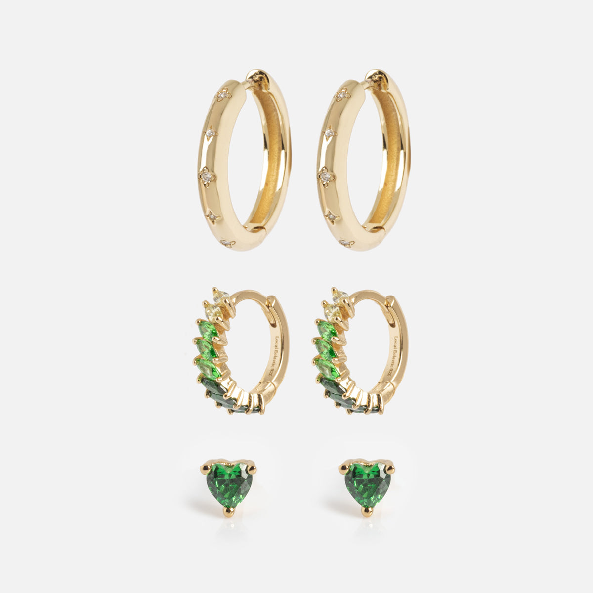 The Bold Birthstone Earring Set includes three pairs: plain gold hoops with small gemstones, gold hoops with green gradient stones, and stud earrings featuring heart-shaped green gems, all on a white background.