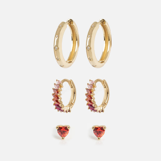 The Bold Birthstone Earring Set features three gold pairs: diamond-accented hoops, pink and red gemstone hoops, and heart-shaped red gemstone studs, all shown vertically against a white background.