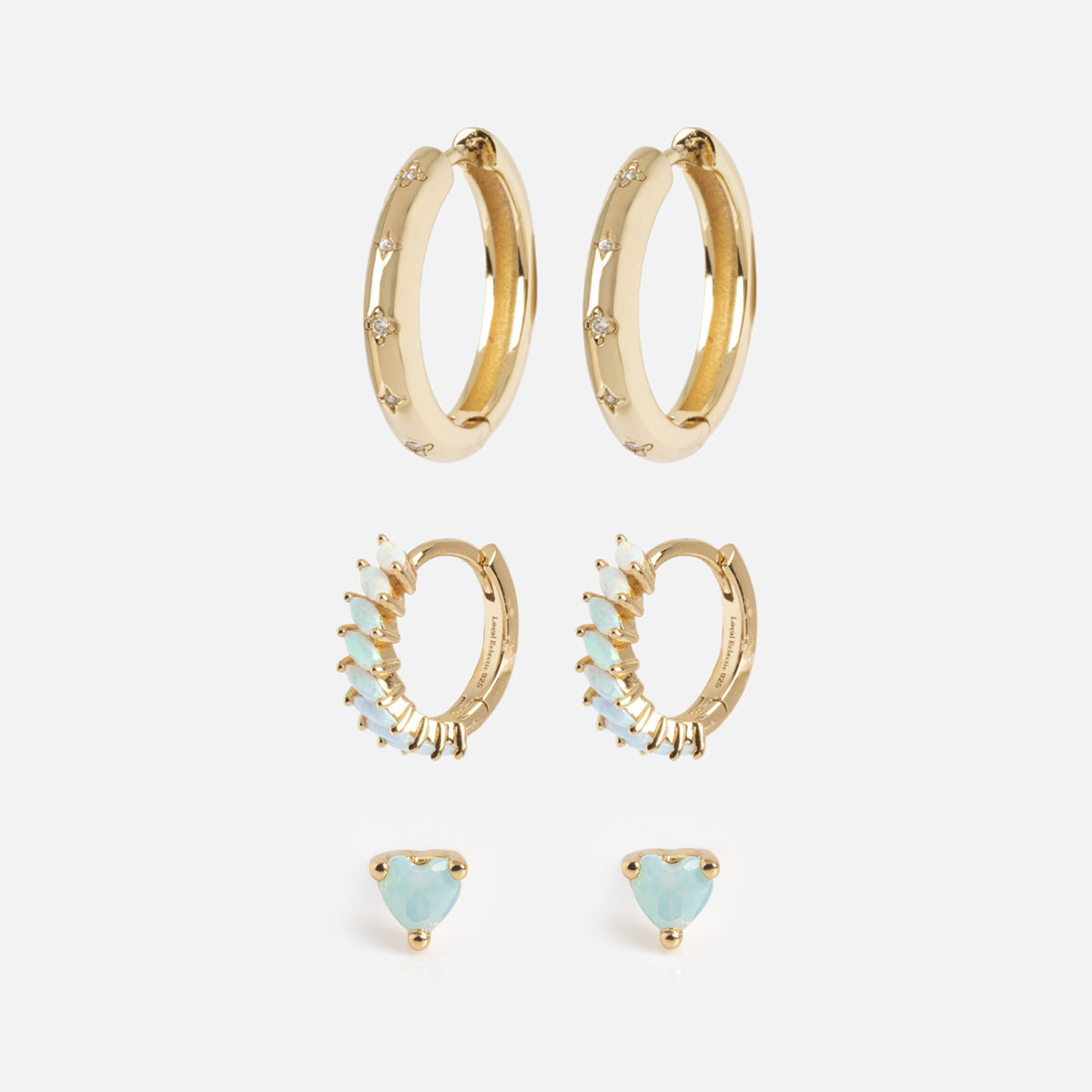 The Bold Birthstone Earring Set includes three pairs: plain gold hoops with small gems, gold hoop earrings with blue opal stones, and small blue opal studs in a triangular setting, all displayed on a white background.