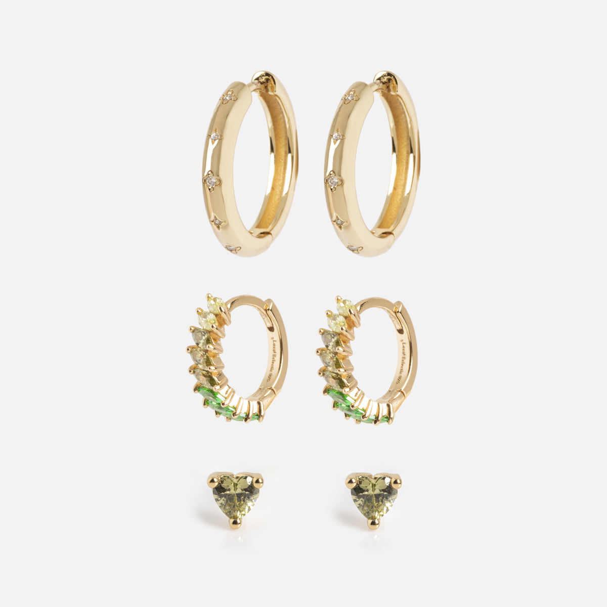 The Bold Birthstone Earring Set features three pairs of gold earrings: smooth hoops with tiny stones, hoops accented with green and clear stones, and small studs with green heart-shaped gems, all shown on a white background.