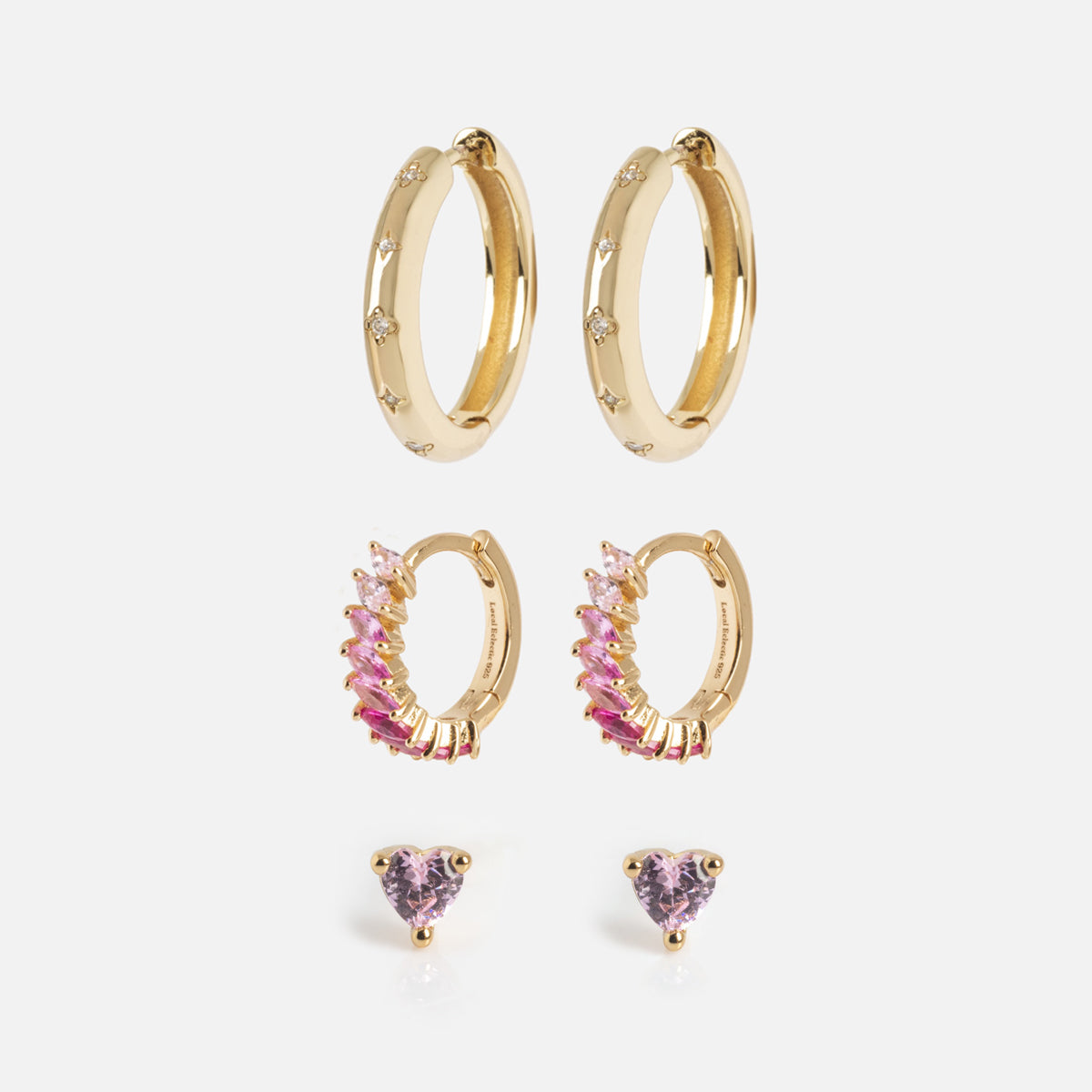 The Bold Birthstone Earring Set features three gold pairs: round hoops with small stones, marquise-shaped earrings with pink and purple stones, and small studs with purple heart-shaped stones—all displayed on a white background.