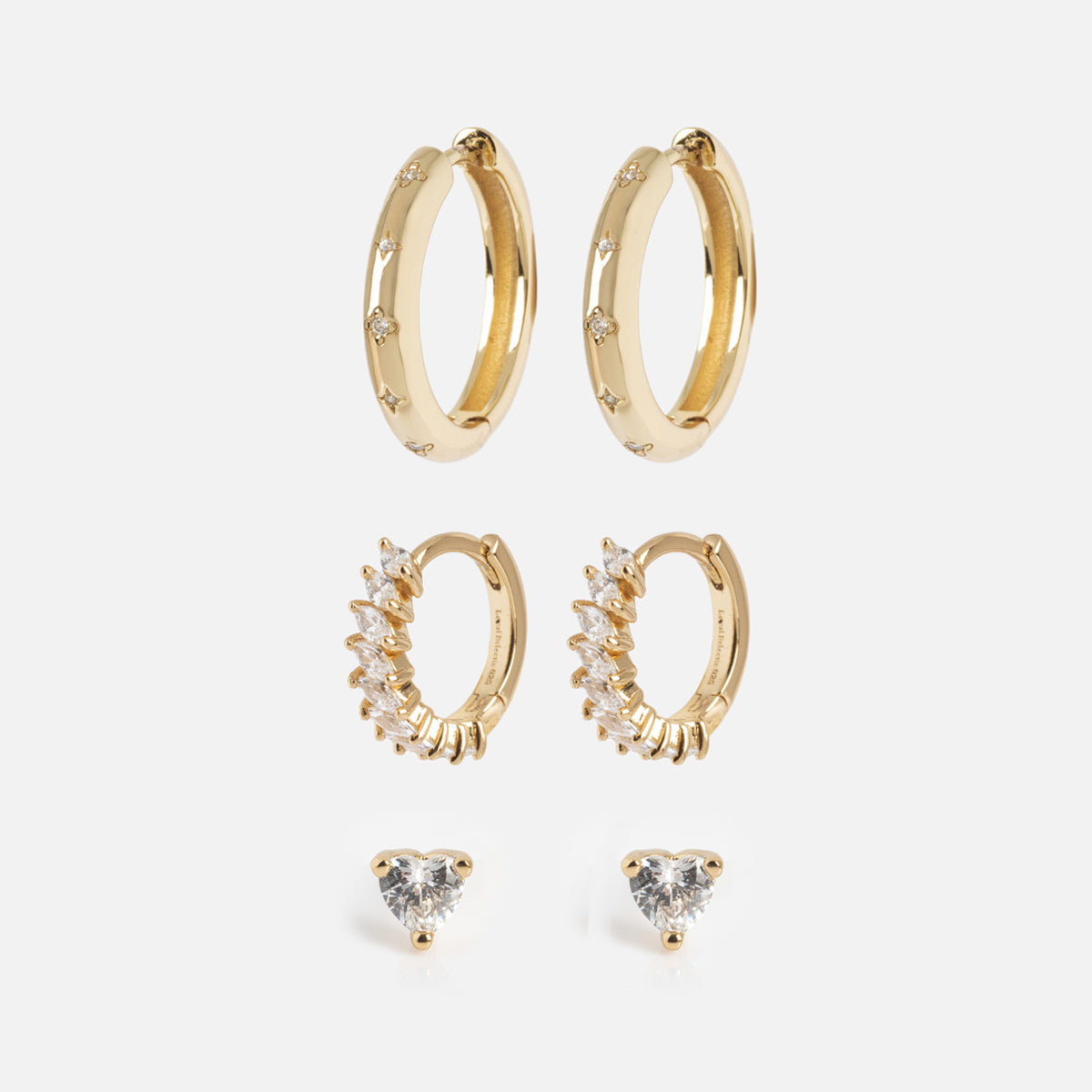 The Bold Birthstone Earring Set features three pairs: plain gold hoops with small embedded gems, gold hoops with a row of marquise-cut gemstones, and heart-shaped gemstone studs, all arranged vertically on a white background.