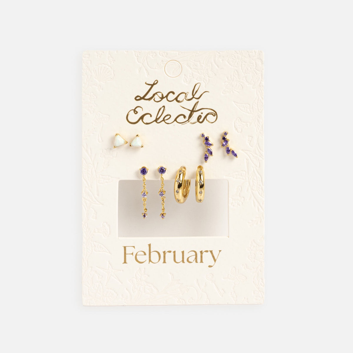 The Classic Birthstone Earring Set features five pairs of 14k gold plated and purple birthstone earrings—studs, hoops, and dangles—displayed on an embossed white “Local Eclectic” “February” card for a personalized ear stack.