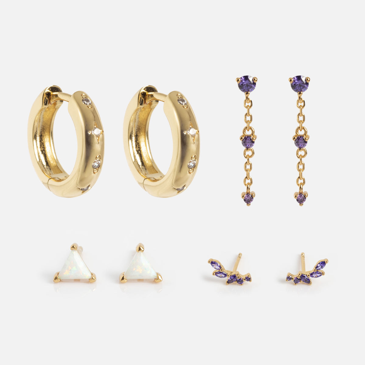 The Classic Birthstone Earring Set features five pairs: chunky gold crystal hoops, dangling earrings with purple stones, white triangular studs, and two unique pairs of small purple stone studs.