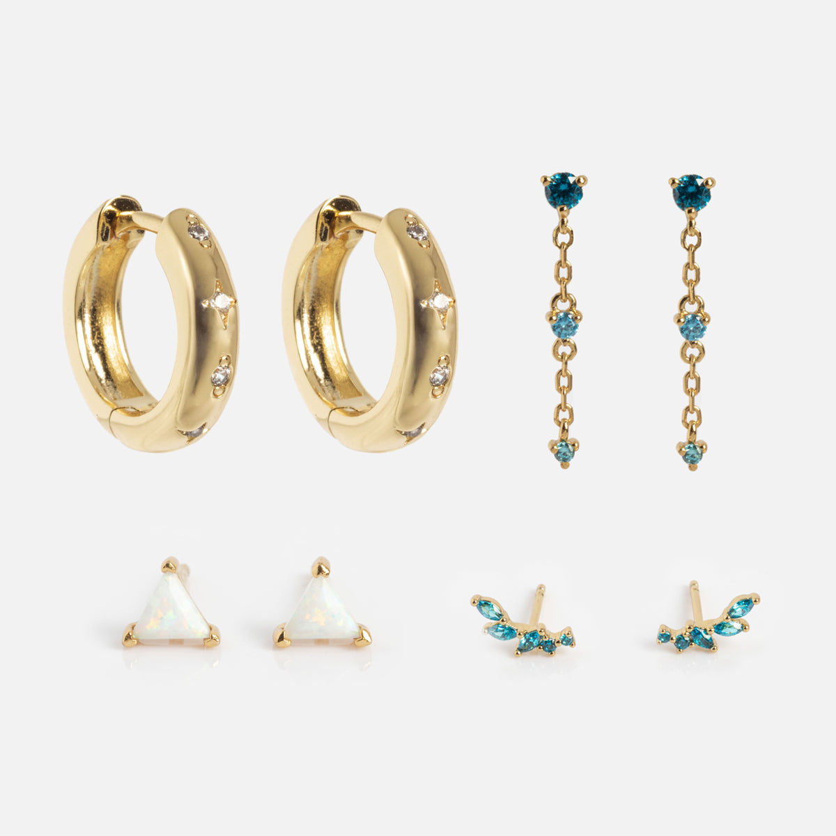 The Bold Birthstone Earring Set includes five pairs: chunky gold hoops with small gemstones, blue gemstone chain drops, white triangle studs, blue gemstone wing-shaped studs, and small blue gemstone studs on a white background.