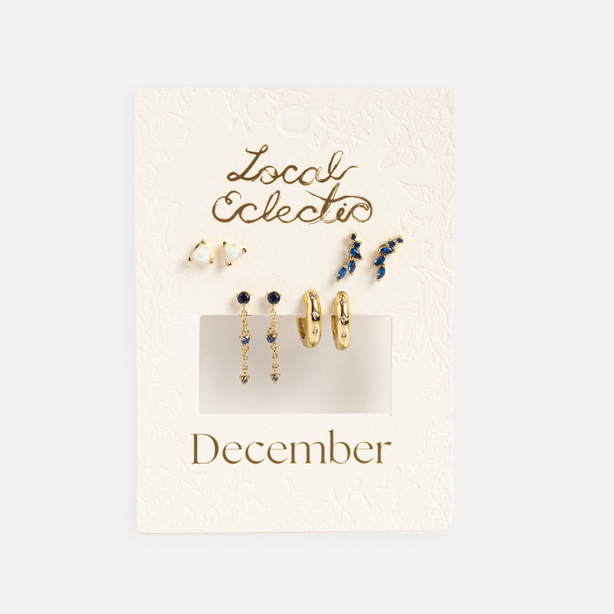 The Classic Birthstone Earring Set features six pairs of 14k gold plated gold and blue studs, hoops, and dangles on a textured white jewelry card—perfect for creating a personalized ear stack.