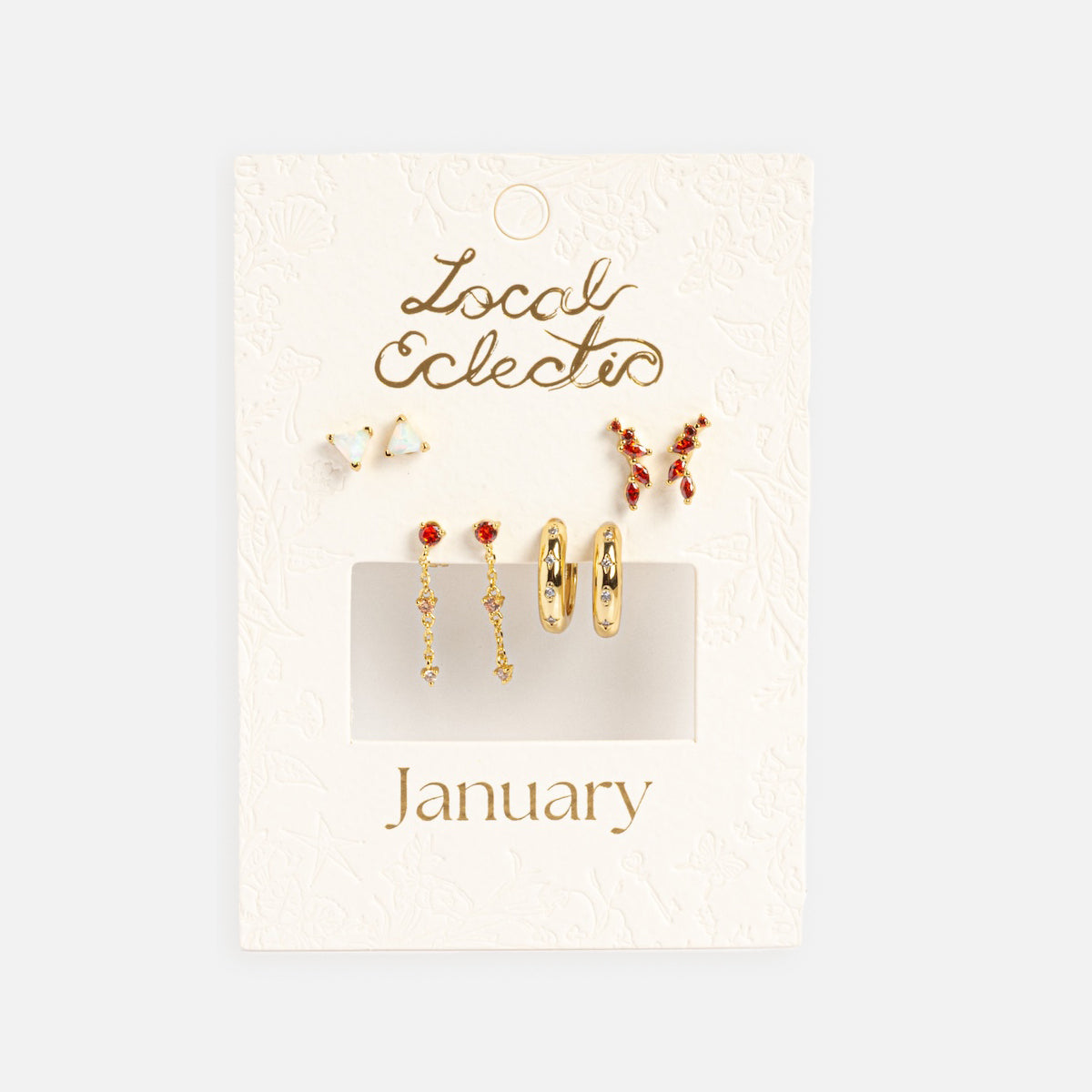 A white textured card labeled Local Eclectic January displays the Classic Birthstone Earring Set, a 14k gold-plated red ear stack featuring five pairs—studs, hoops, and dangles—neatly arranged on a light background.