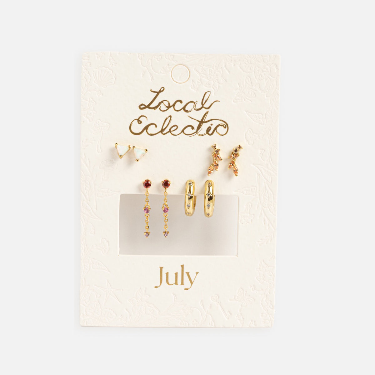 The Classic Birthstone Earring Set features five pairs of 14k gold plated earrings with red and pink stones, displayed on an embossed white card labeled Local Eclectic x July—ideal for personalizing your ear stack.