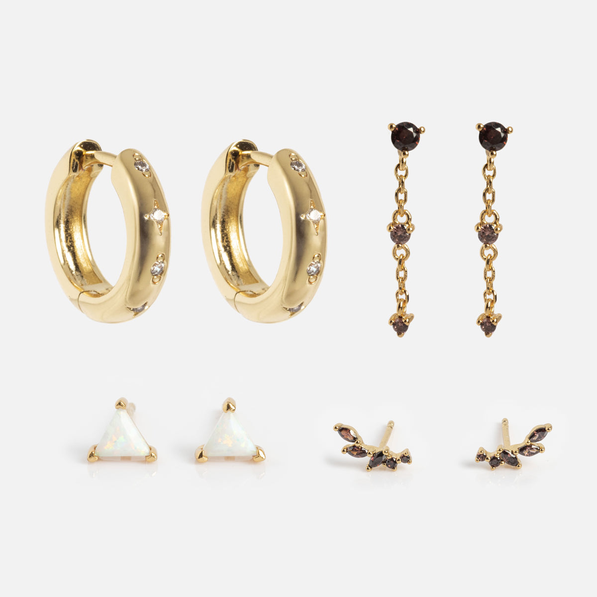 The Bold Birthstone Earring Set features four pairs: chunky gold crystal hoops, dangling earrings with three dark stones, triangle opal studs, and butterfly-shaped stud earrings adorned with dark stones.