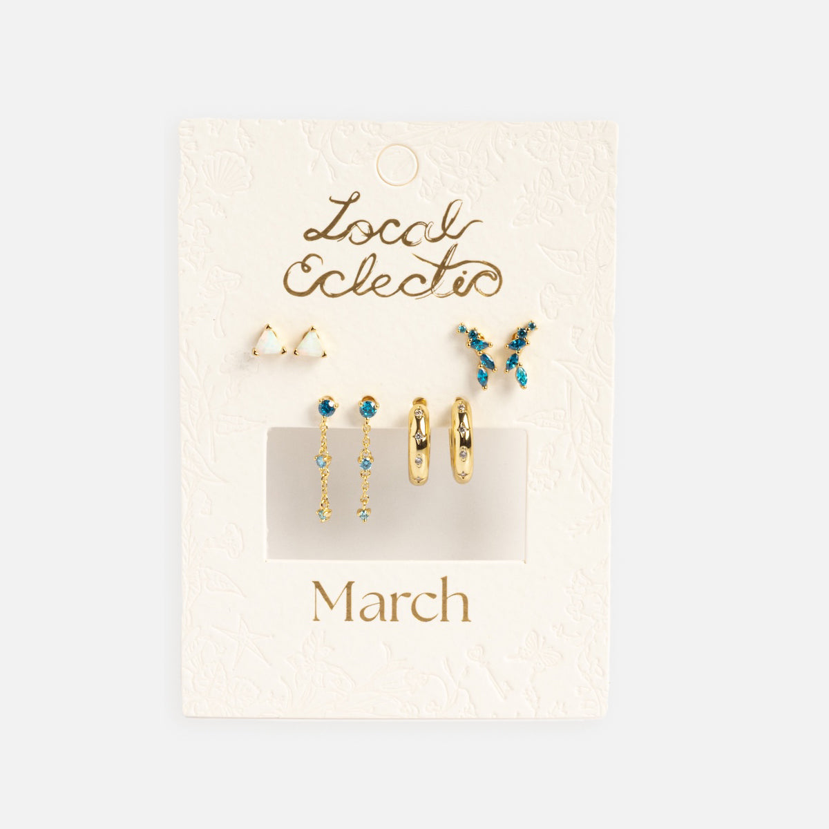 The Classic Birthstone Earring Set features five pairs of 14k gold plated earrings with blue and white stones, ideal for a personalized ear stack, displayed on a textured white card labeled Local Eclectic and March in gold.