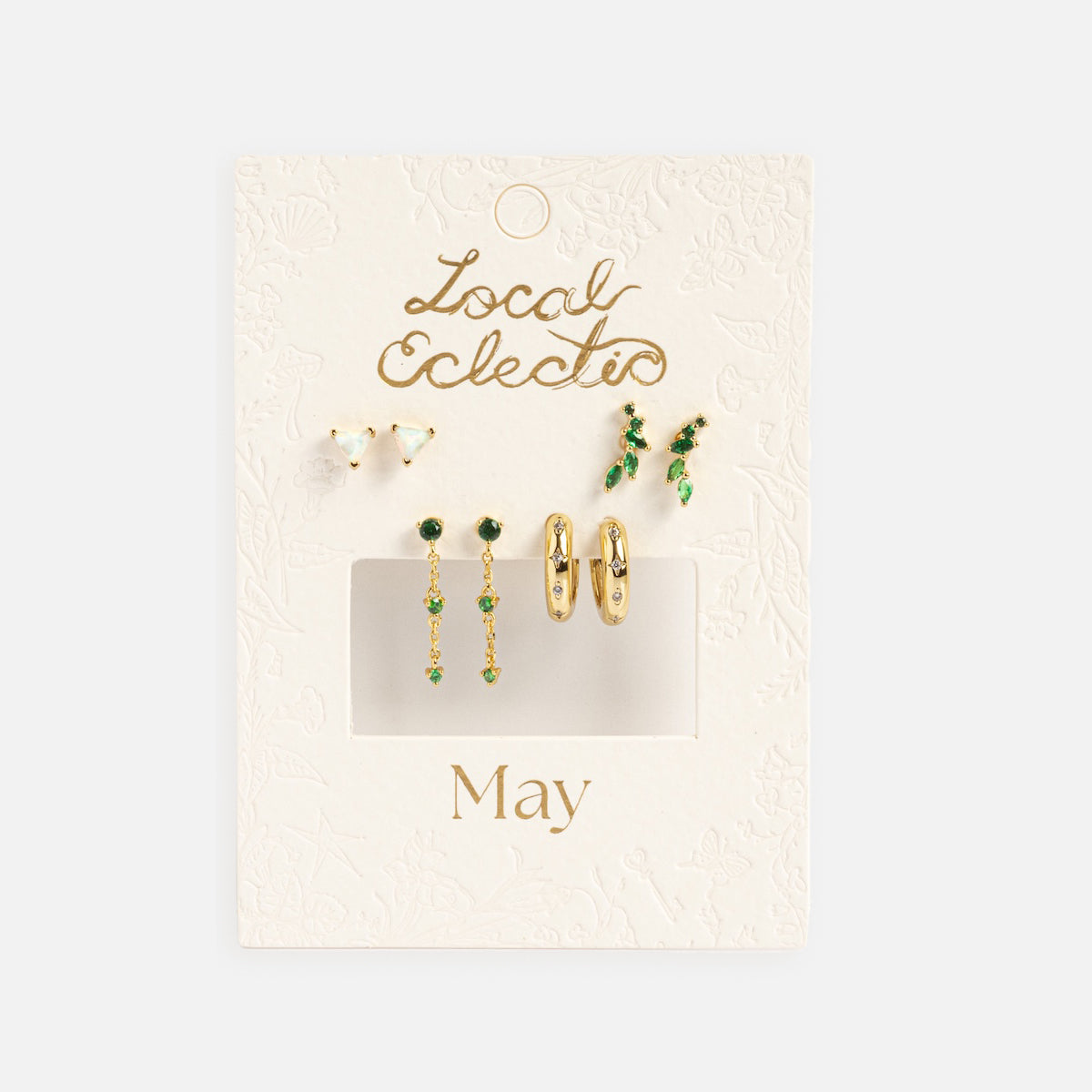 The Classic Birthstone Earring Set features five pairs of 14k gold-plated green and gold earrings on a textured white card labeled "Local Eclectic" and "May." Includes studs, hoops, and drops—perfect for a personalized ear stack.