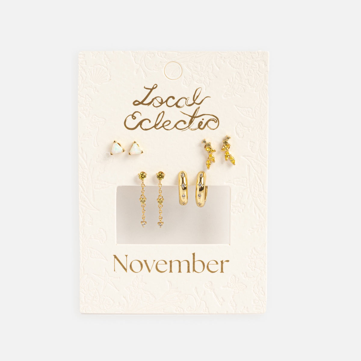 The Classic Birthstone Earring Set features 14k gold plated studs, drop earrings, and small hoops with yellow gemstones, displayed on a cream Local Eclectic card labeled November. This set is a personalized ear stack.