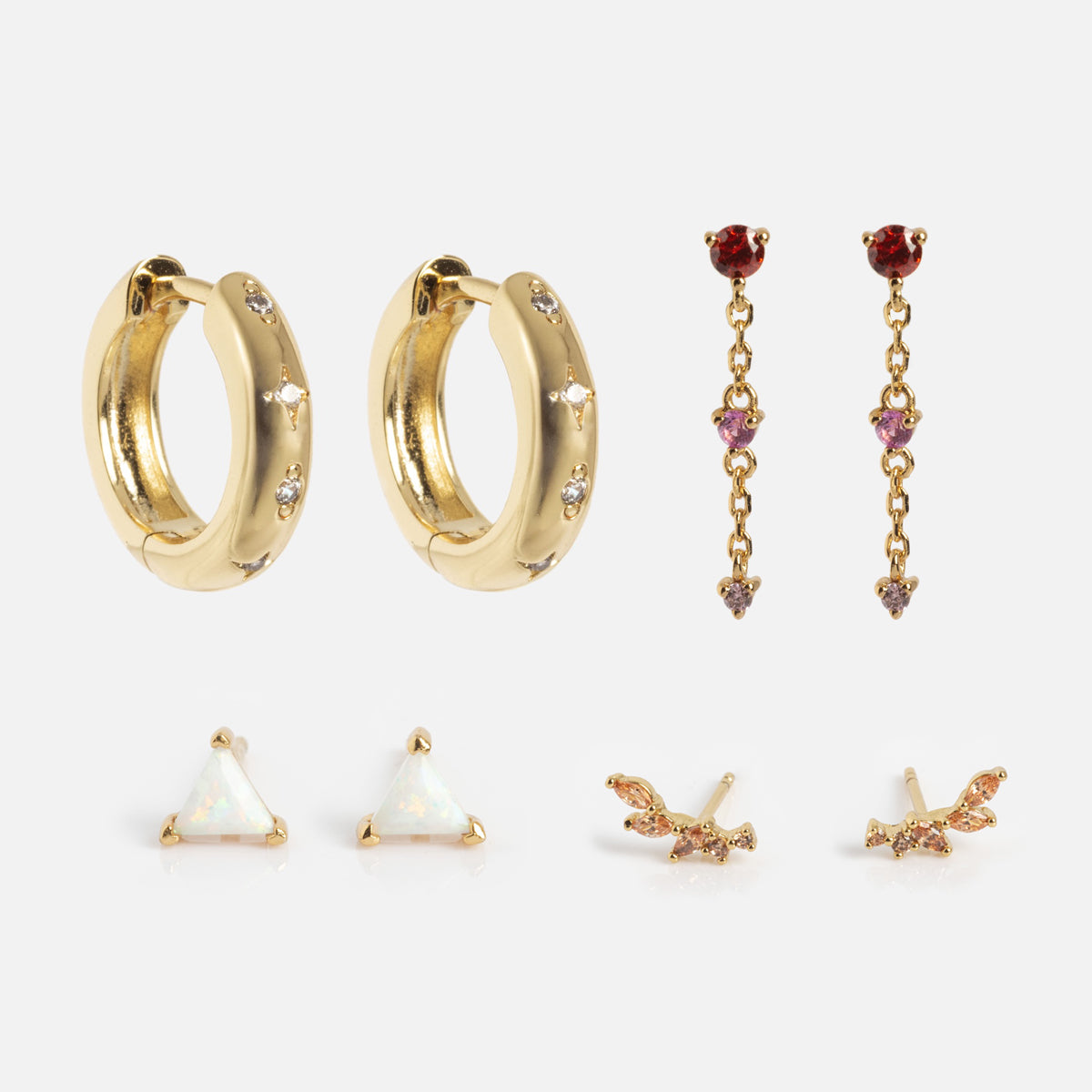 The Bold Birthstone Earring Set includes five gold earrings: chunky hoops with gemstones, dangly earrings with red and pink gems, white triangular studs, wing-shaped studs, and tiny bird studs.