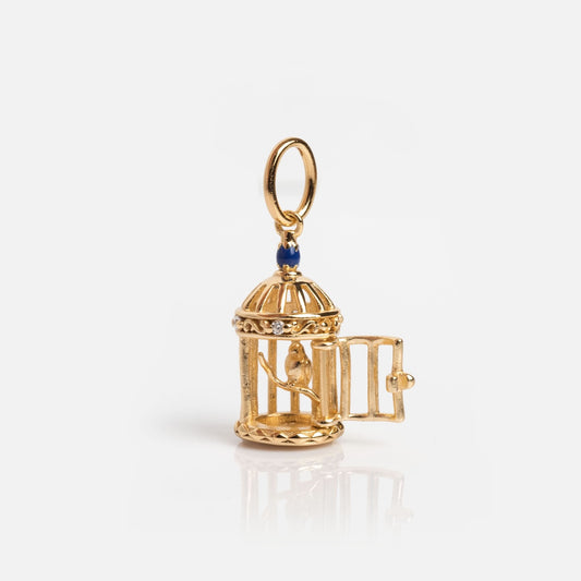 The Vintage Inspired Trinket Charm is a gold birdcage with a tiny bird inside, an open door, and blue accent at the top. It comes with a hanging loop, making it the perfect gold vermeil accessory for period piece lovers.