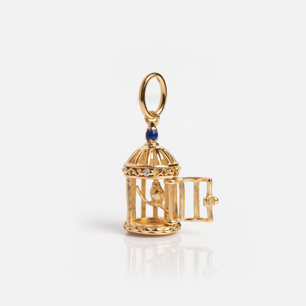 The Vintage Inspired Trinket Charm is a gold birdcage with a tiny bird inside, an open door, and blue accent at the top. It comes with a hanging loop, making it the perfect gold vermeil accessory for period piece lovers.
