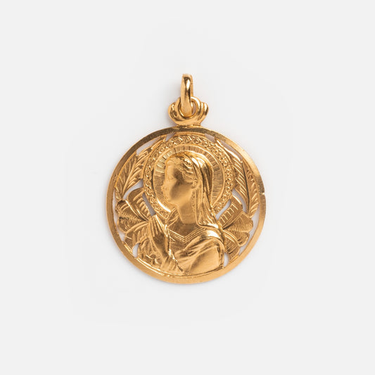 The Vintage 18k Ornate Openwork Mother Mary Coin Charm features an engraved profile of Mary with a halo, hands in prayer, and intricate Art Nouveau-inspired background designs.