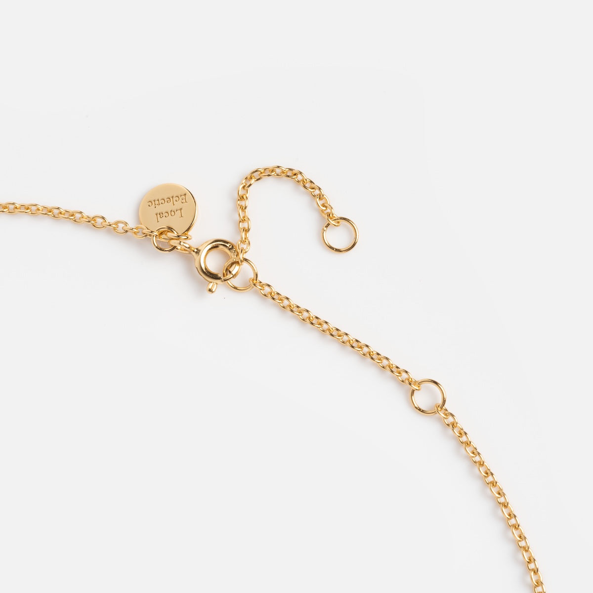 A close-up of the Forget Me Not Blue Topaz Memento Necklace, a delicate gold vermeil piece featuring a lobster clasp, extender chain, and a small round engraved tag, shown on a white background.